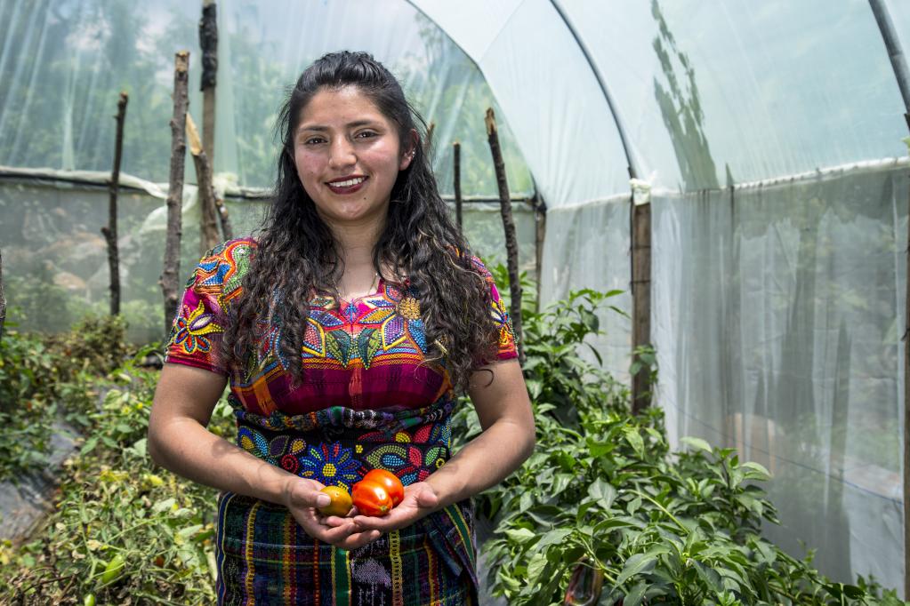 La joven Marisela Ambrosio sostiene unos tomates, dentro de un invernadero