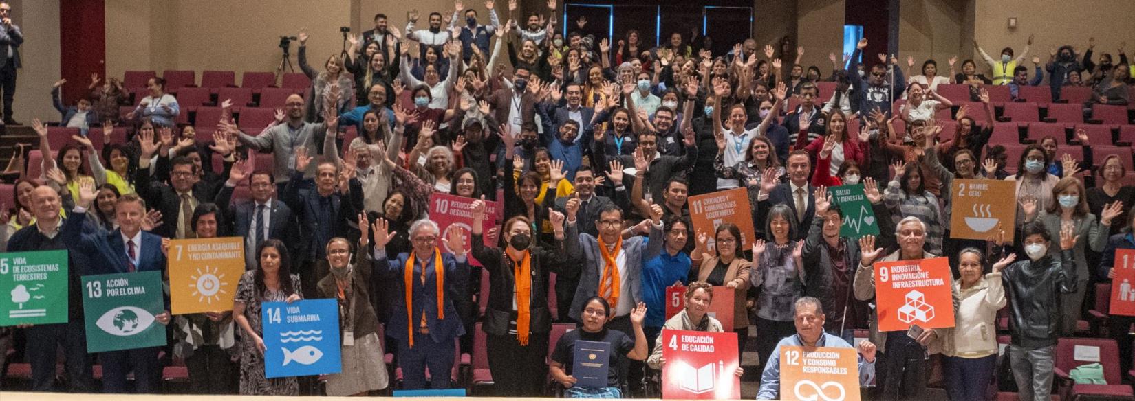 Muchas personas que asistieron al teatro del Museo del Niño, saludan alegremente con símbolos de los ODS, luego de los actos del día de las personas con discapacidad.