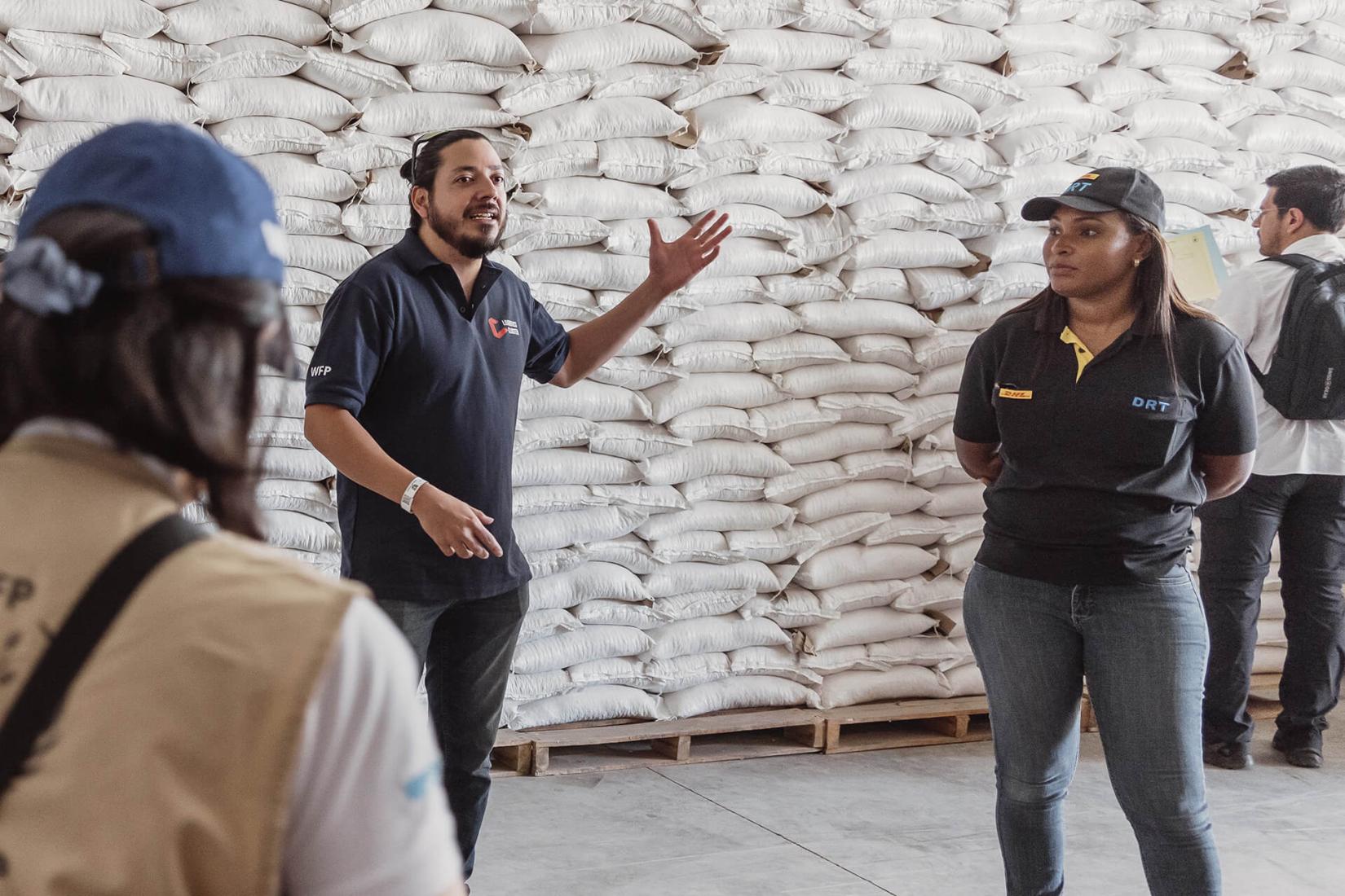 Personas paradas frente a unos sacos de granos estibados hasta arriba