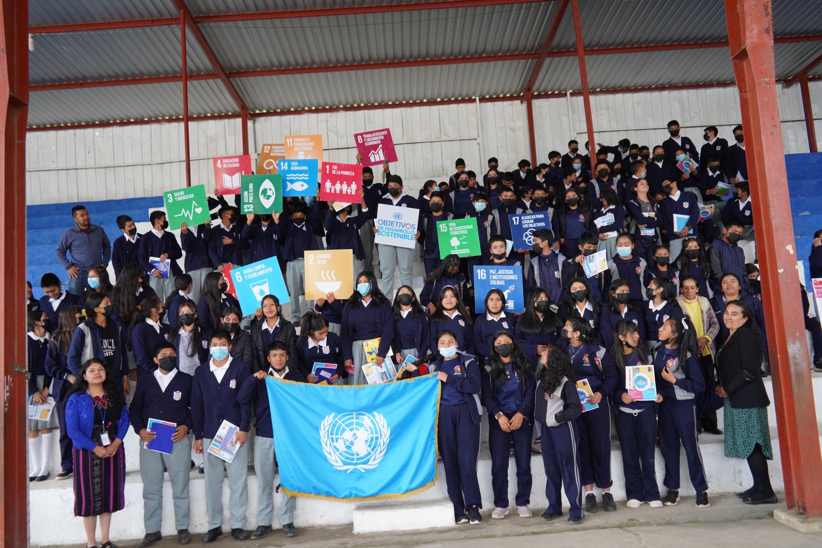 Jovenes estudiantes sostienen la bandera de la ONU y carteles de los ODS, en una capacitación 