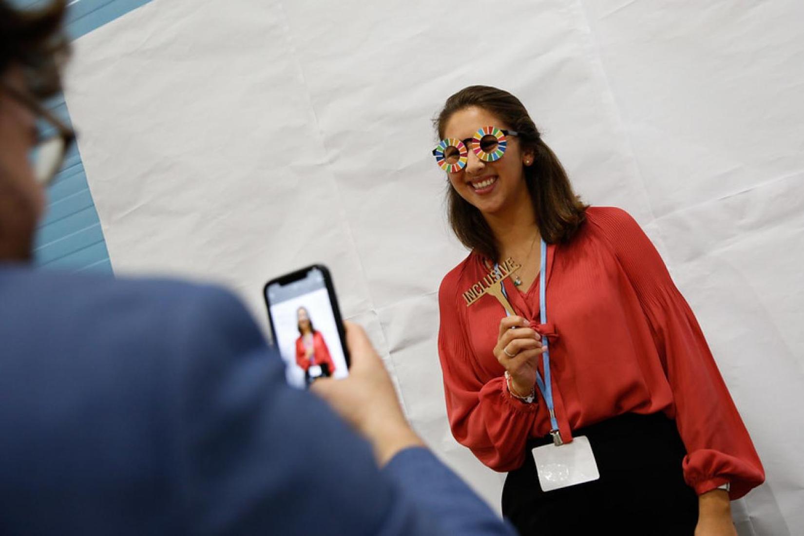 Joven mujer con camisa roja posa para una foto con gafas temáticas de los ODS Pie de foto: El Día Internacional de la Juventud de este año se celebrará bajo el tema de Habilidades Verdes para la Juventud: Hacia un Mundo Sostenible. Foto: © PNUD