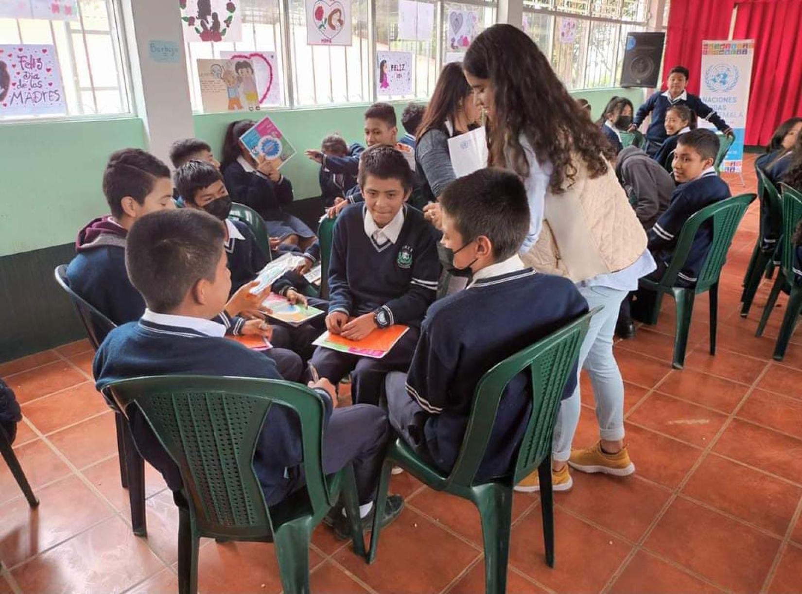 Sofia de pie, entrega materiales a jóvenes sentados en círculos de trabajo en su salón de clases