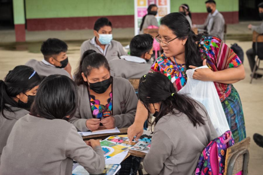 Mujeres jóvenes sentadas, revisando materiales de ODS mientras Zully, de pie, les explica