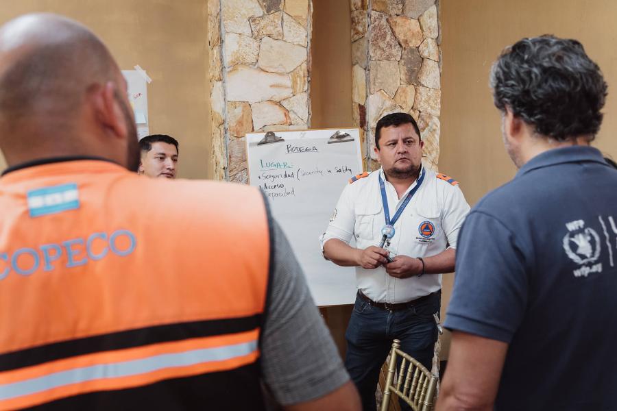 Dos particiantes miran hacia un participantes que está por escribir en un rotafolio