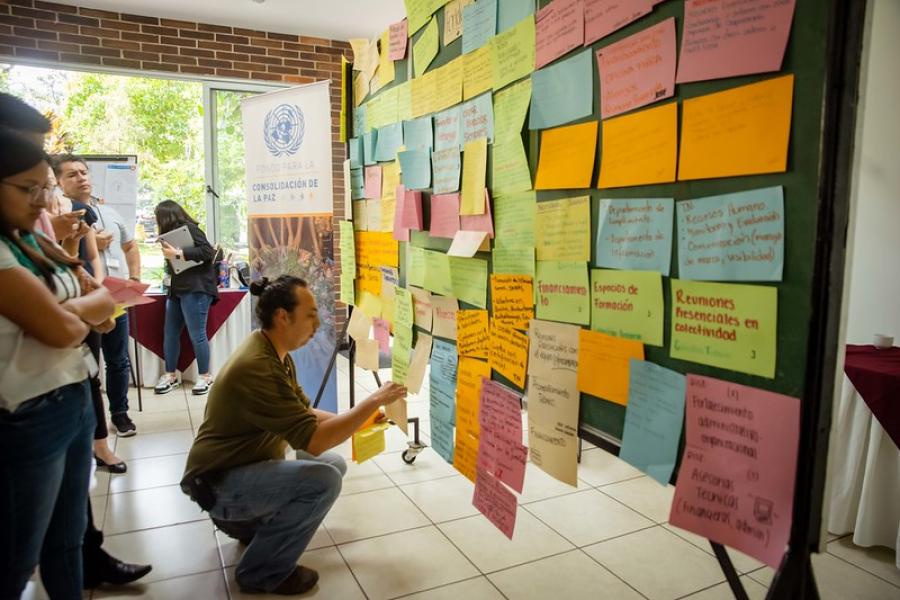Joven pega tarjetas en una pared donde hay más tarjetas con ideas sobre prioridades de la juventud en un taller del Fondo de Consolidación de la Paz (PBF)