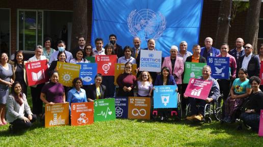 Miembros del Consejo, en el jardín de Casa de la Asunción, sosteniendo símbolos de los ODS, detrás del grupo la bandera de la ONU.