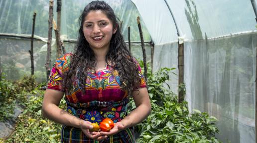 La joven Marisela Ambrosio sostiene unos tomates, dentro de un invernadero